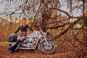 red-haired female biker in the autumn forest at sunset