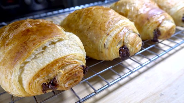 Closeup circular dolly shot of a row of oven baked pain au chocolat pastries / cholcolate croissants resting on a cooling grid.