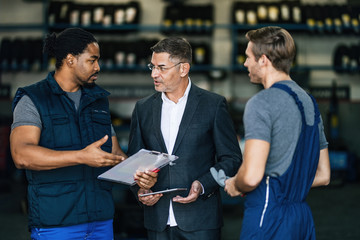 Car mechanics and manager discussing about reports in auto repair shop.