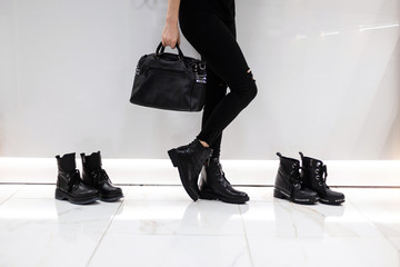 Young woman with a fashionable black leather bag in stylish boots in jeans stands near a white wall...