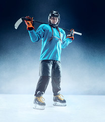 Young female hockey player with the stick on ice court and blue background. Sportswoman wearing...