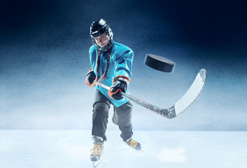 Young female hockey player with the stick on ice court and blue background. Sportswoman wearing...