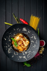 Meat lasagna with beef and tomato sauce on a black plate on a dark wooden background. The concept of Italian cuisine