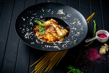 Meat lasagna with beef and tomato sauce on a black plate on a dark wooden background. The concept of Italian cuisine