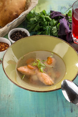 clear vegetable soup with salmon in green bowl on blue wooden table