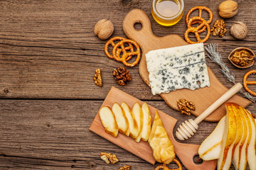 Cheese plate antipasti with smoked and blue cheese, crackers, honey, walnuts and ripe pear. Traditional snack recipe idea. Wooden boards background