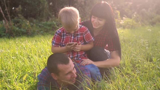 happy family teamwork lifestyle outdoors have fun concept outdoors slow motion video . mom dad and son take a photo with a smartphone in nature are sitting on the grass have fun playing .mom girl dad