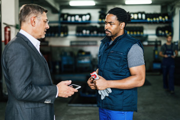 African American auto mechanic talking to his manager in repair shop.