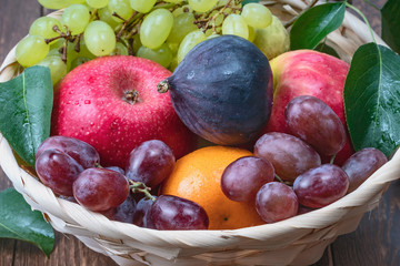 red and white grapes and fresh fruits in a straw basket on a dark wooden background