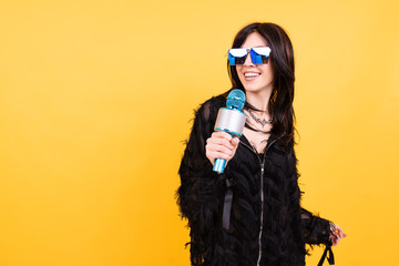 Obraz premium Beautiful young woman in glasses and with microphone on yellow background