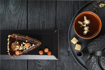Black teapot and green tea with jasmine in a clay cup, on a black and wooden background with a slice of cake. Food concept. Top view
