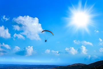  Paraglider is flying over the high mountains. Paragliding on beautiful sky background