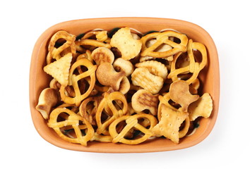 Salty cracker and pretzel snacks, party mix in clay bowl, isolated on white background, top view