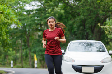 Woman runner at the public road for training in front of a white car.