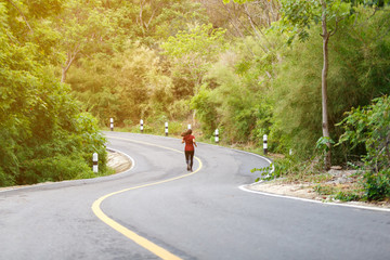 Back of woman runner and runing at the road surround with green forest.