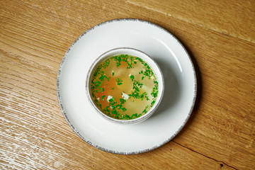 Dietary soup with chicken, vegetables and parsley on wooden background in white bowl. Top view tasty soup. Flat lay food