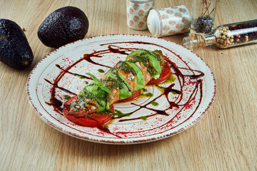Fried avocado and chicken with tomatoes and mozzarella on a white plate. Delicious diet and healthy food. Close up. wooden background