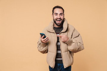 Image of unshaven man in winter jacket smiling and holding smartphone