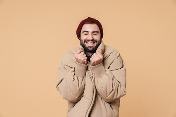 Image of handsome young man in winter jacket and hat smiling at camera
