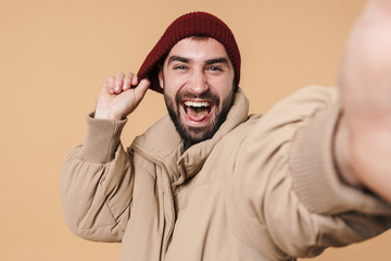 Image of man in winter jacket and hat smiling while taking selfie photo