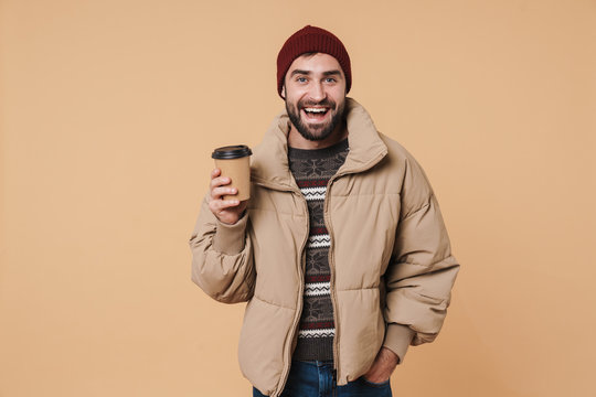 Image of young man in winter jacket and hat smiling while drinking coffee