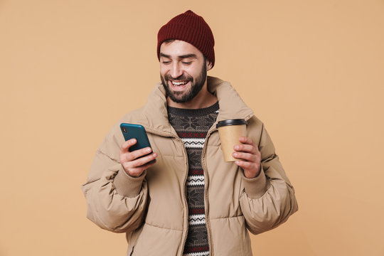 Image of young man in winter clothes holding coffee cup and cellphone