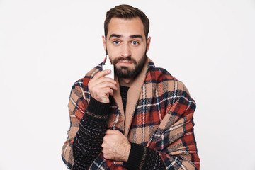Portrait of ill guy wrapped in blanket holding nose drops due to flu