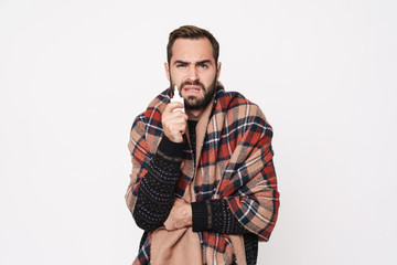 Portrait of ill guy wrapped in blanket holding nose drops due to flu