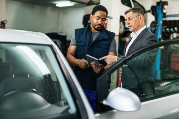 Young black car mechanic using touchpad with his customer in a repair shop.