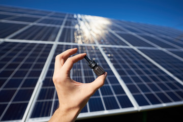 Man's hand keeping tiny detail for solar battery installing in front of solar pannel on background....