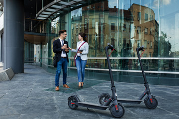 Two business people with electric scooter talking outside in front of modern business building.
