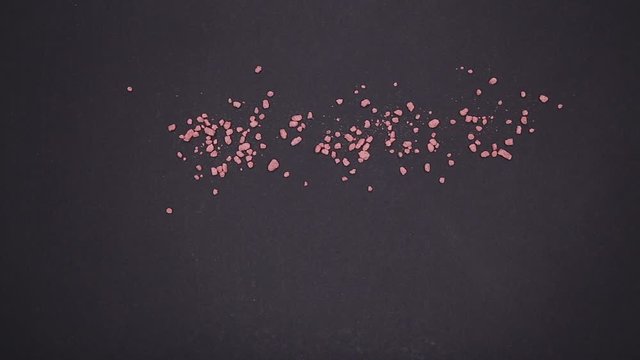 Small pink and yellow grains scatter on a black table with a male hand