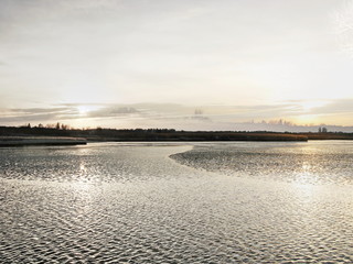 The mixed image of the view of the ice on the surface of the lake and the natural background of the view of the lake shore at the cold spring day at the City Park. 