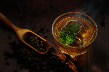 Still life of hot tea with smoke with peppermint on wooden table, shooting in studio. Low key toned image. Free space for text. Good drink for healthy ideas concept for advertising. Selective focus.