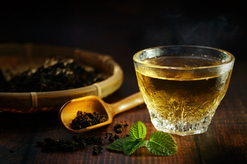 Still life of hot tea with smoke with peppermint on wooden table, shooting in studio. Low key toned image. Free space for text. Good drink for healthy ideas concept for advertising. Selective focus.
