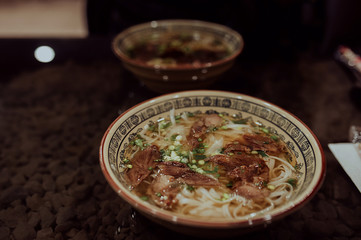 a large plate of Vietnamese hot pho bo soup on a dark table, in the background another plate of soup