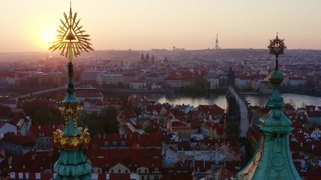 Aerial view St. Nicholas church and mala strana district in Prague at sunrise. Drone flying at low above roof of famous cathedral, moving down near spire, sun shining through masonic symbol on top. 