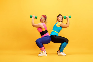 Young caucasian plus size female models training on yellow background. Copyspace. Concept of sport, healthy lifestyle, body positive, fashion. Friendship, girl power. Stylish woman practicing, smiling