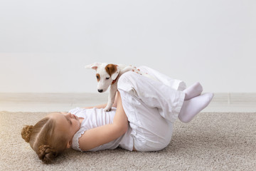Children, pets and dogs concept - Little adorable child girl lying on the floor and playing with funny puppy Jack Russell Terrier