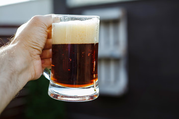 Young man holds a glass of beer in his hand, on a black background.