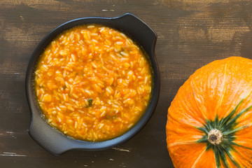 Rice in pumpkin sauce on black plate on wooden background