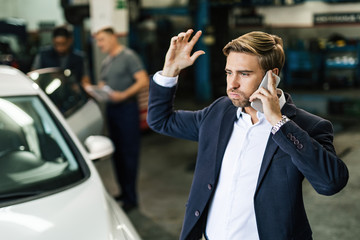 Frustrated businessman talking on mobile phone in auto repair shop.