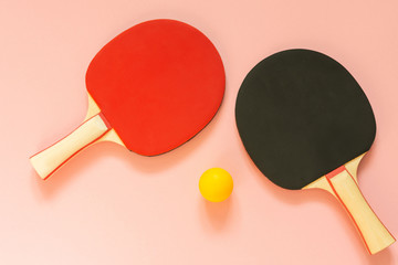 Black and red tennis ping pong rackets and orange ball isolated on a pink background, sport...