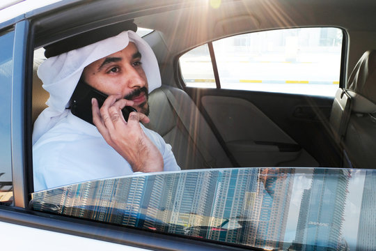 Emirati man using smart mobile phone. Arab Middle Eastern guy in the UAE wearing Kandura while seating on car's backseat calling someone as mock up