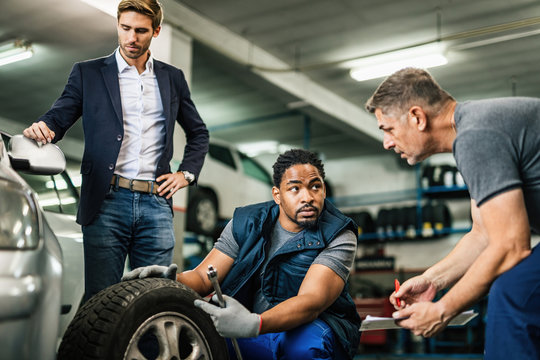 African American mechanic and his coworker examining customer's car tire at repair shop.