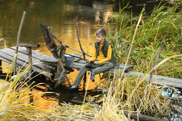 Boy with a fishing net is leaning on a wooden dock railing
