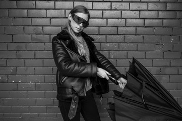 Black and white fashion portrait of stylish girl wearing sheepskin coat and sunglasses with umbrella in her hand and posing against brick wall on background.