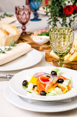 Served for holiday banquet restaurant table with Greek salad, dishes, snack, salads, cutlery, wine and water glasses. European food in a restaurant setting. Table set for an event party. catering