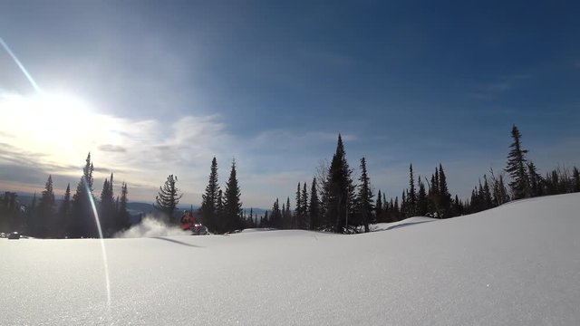 elite snowmobile rider makes a turn and jump. on the background of the winter forest, leaving behind a trail of splashes of white snow. bright snowmobile and suit. snowmobilers sports riding. 4K