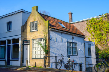 Very small white canal house with a Dutch bicycle against a fence in the foreground.